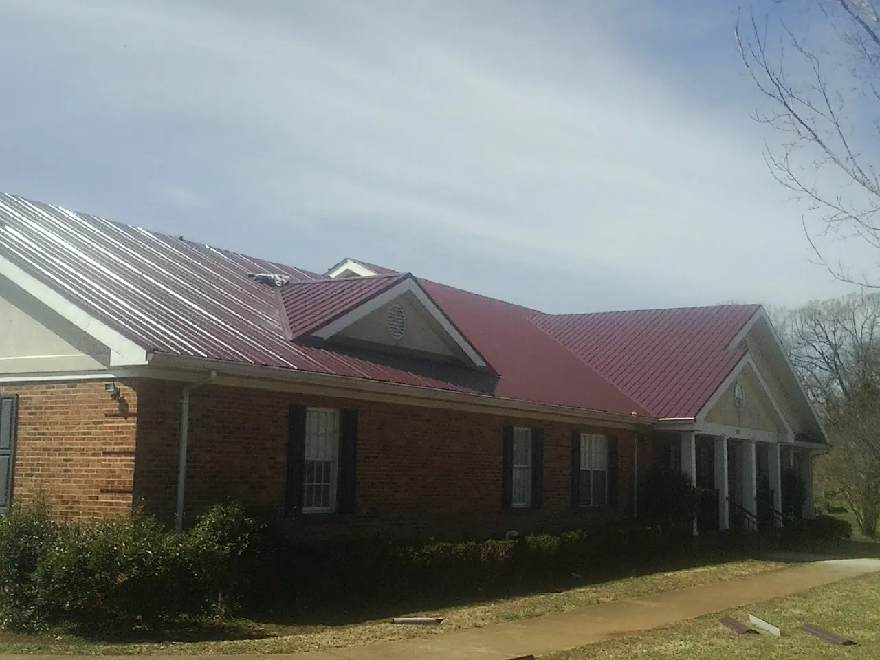 Red metal roof with gabled entries on a long brick building, from a Hail Damage Roof Repair job in Erie