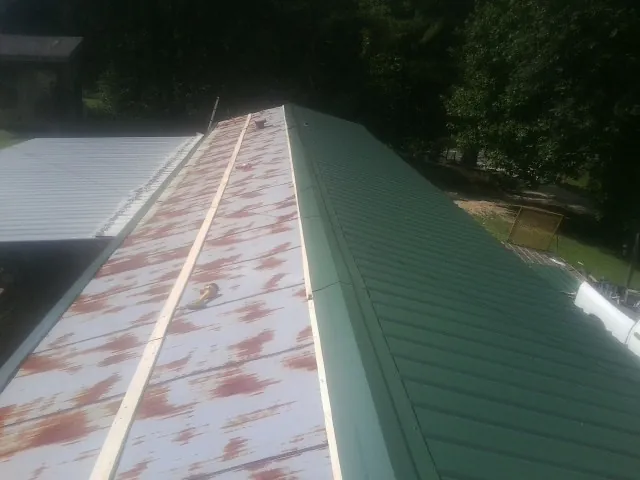 Old rusted panels beside newly installed green metal roofing — Wind Damage Roof Repair by Roofing Brothers in Erie